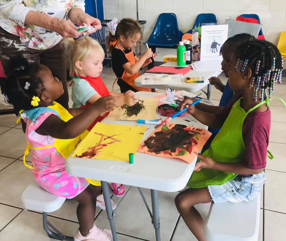 diverse group of children from toddlers- kindergarten age painting at child sized tables. 