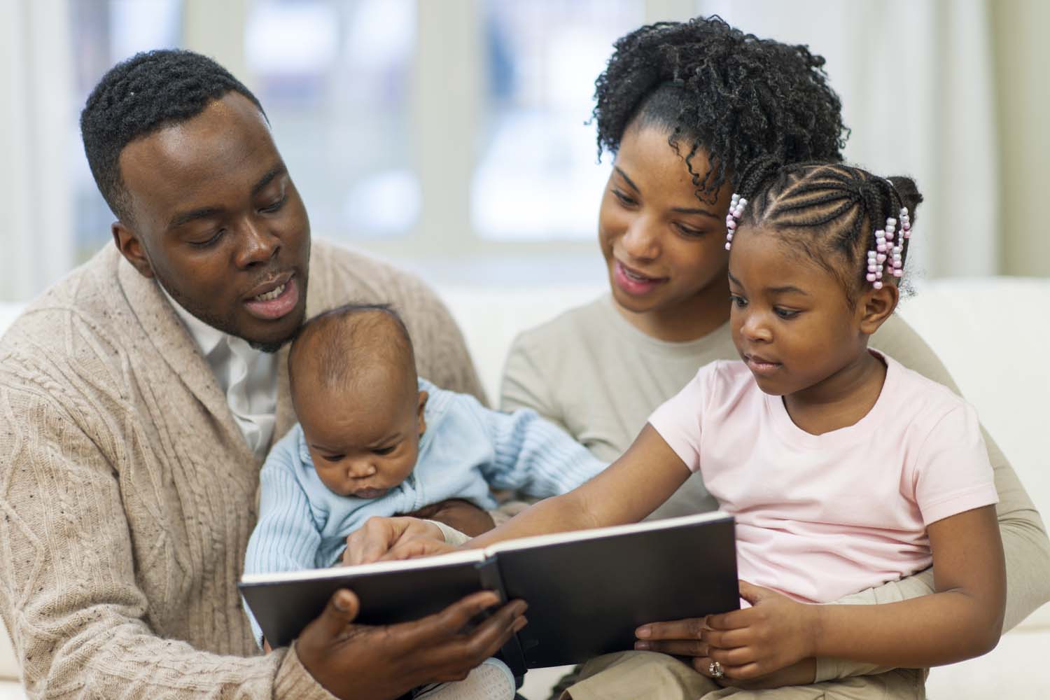 African American father and mother reading to young child and infant
