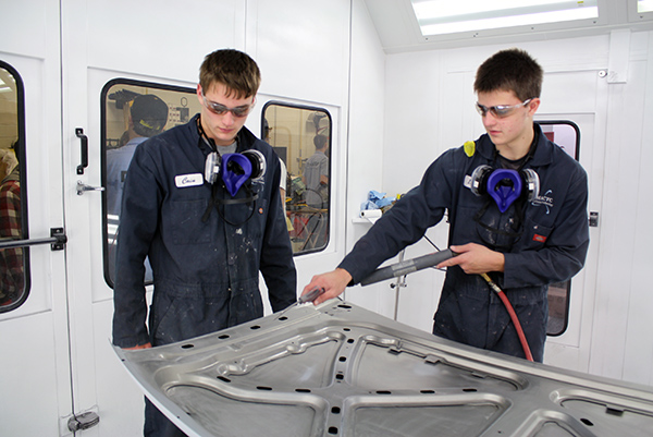 Two students work on the hood of a vehicle inside the paint booth.