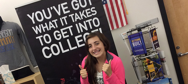 A young lady gives two "thumbs-up" after completing her college application.