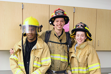 Criminal Justice students, two males and one female, pose in their fire-fighting gear.