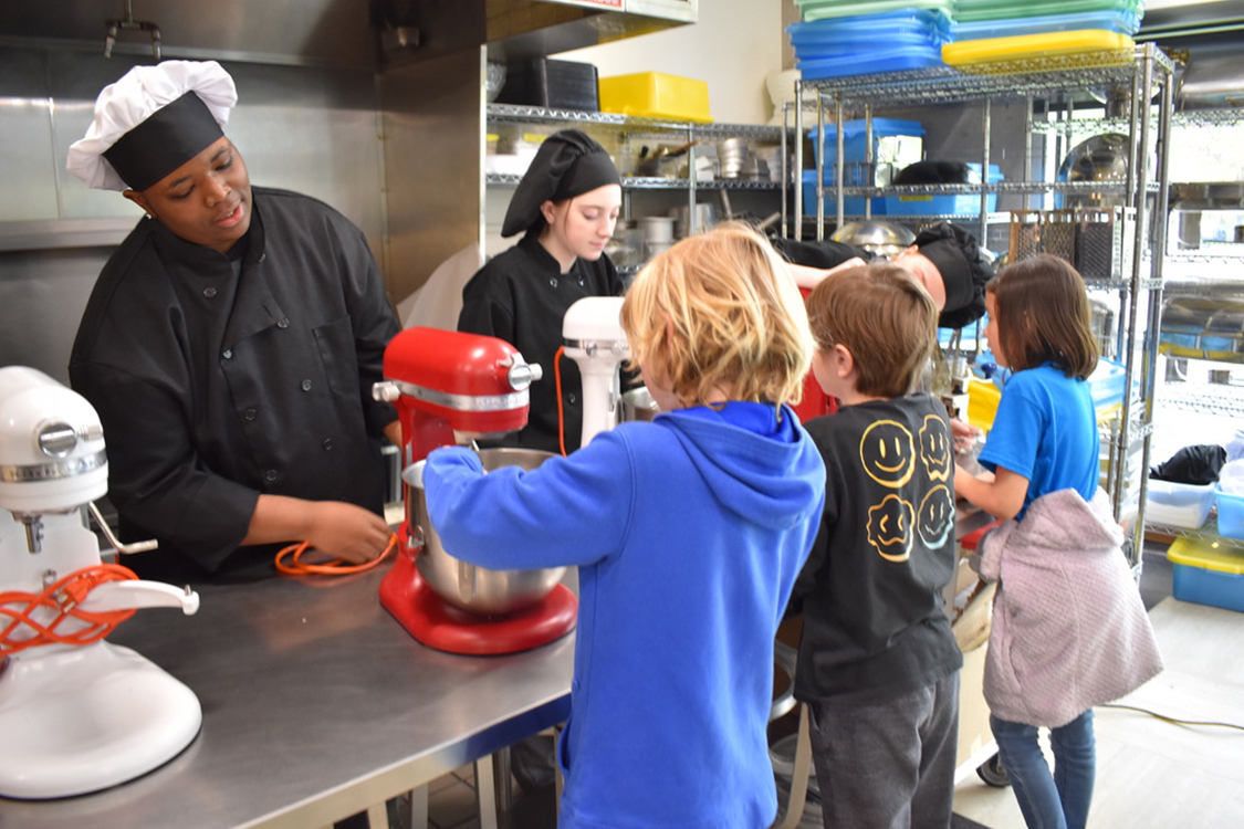 Fourth graders learn to use a mixer with help from high school culinary students