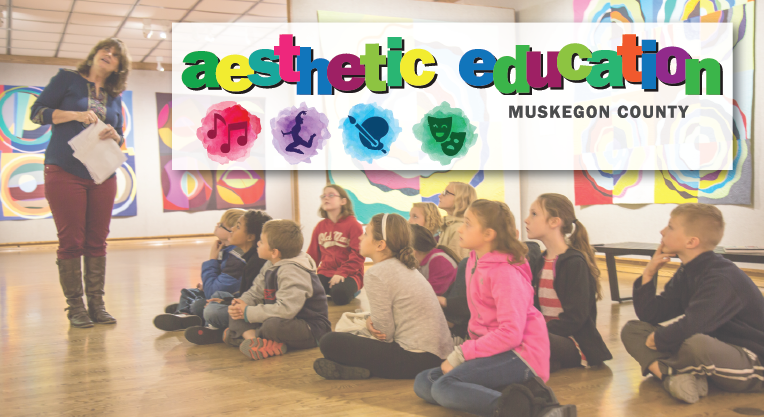 Students discuss artwork at the museum. Aesthetic Education logo with icons for music, dance, visual art, and theatre are superimposed.