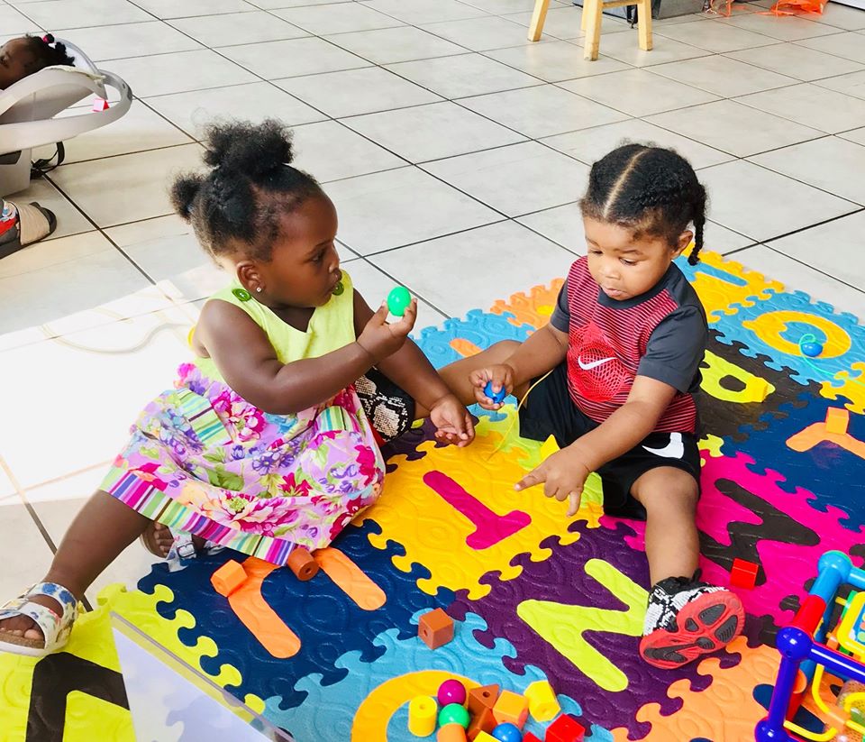 Two babies playing with shaker eggs on a colorful mat at a Great Start Play and Learn Group.  