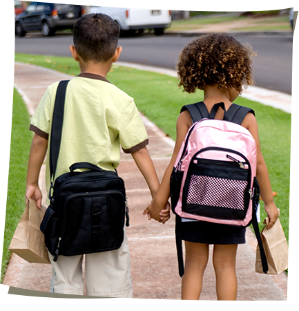Boy and girl with backpacks holding hands and walking down the sidewalk to school