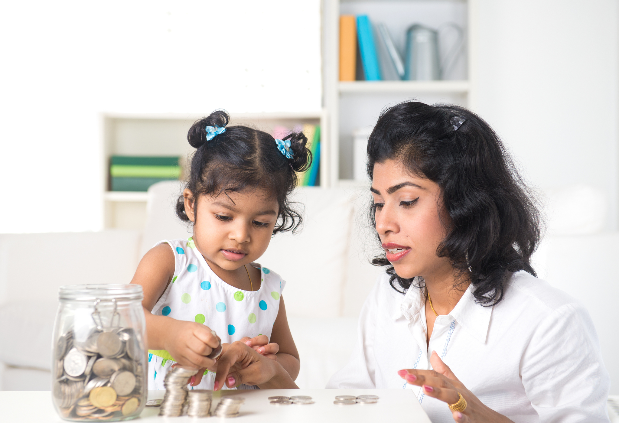Hispanic mother and daughter saving money in a jar