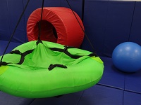 Green saucer shaped swing, hanging from the ceiling. A blue round exercise ball and a large, red, foam tube.