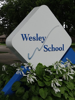 Sign with the Wesley School logo, located in the front parking lot of the school