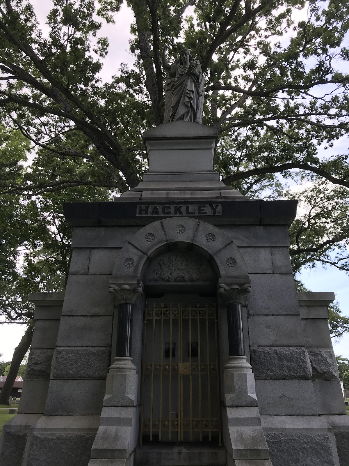 Hackley mousoleum with statue holding book at top, flower details, and columns.